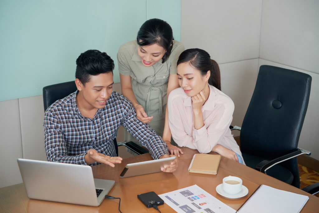 Colleagues sitting and standing around desk and looking at tablet together