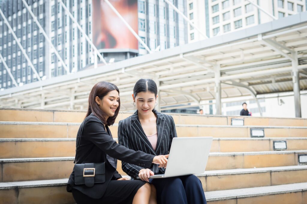 Two women working together outdoors on laptop