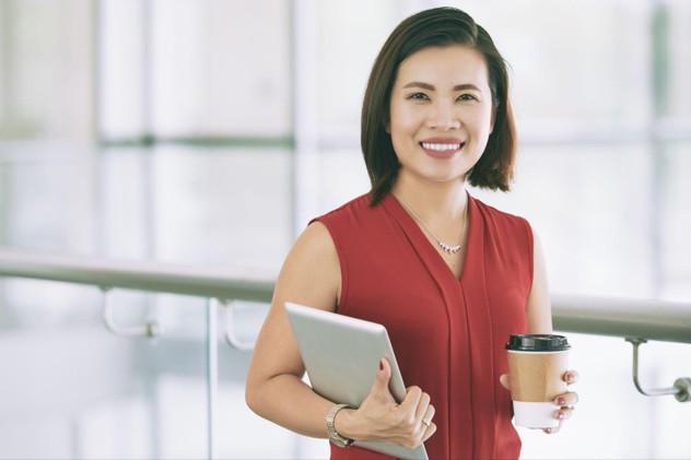 Smiling businesswoman posing indoors balcony with tablet takeaway coffee