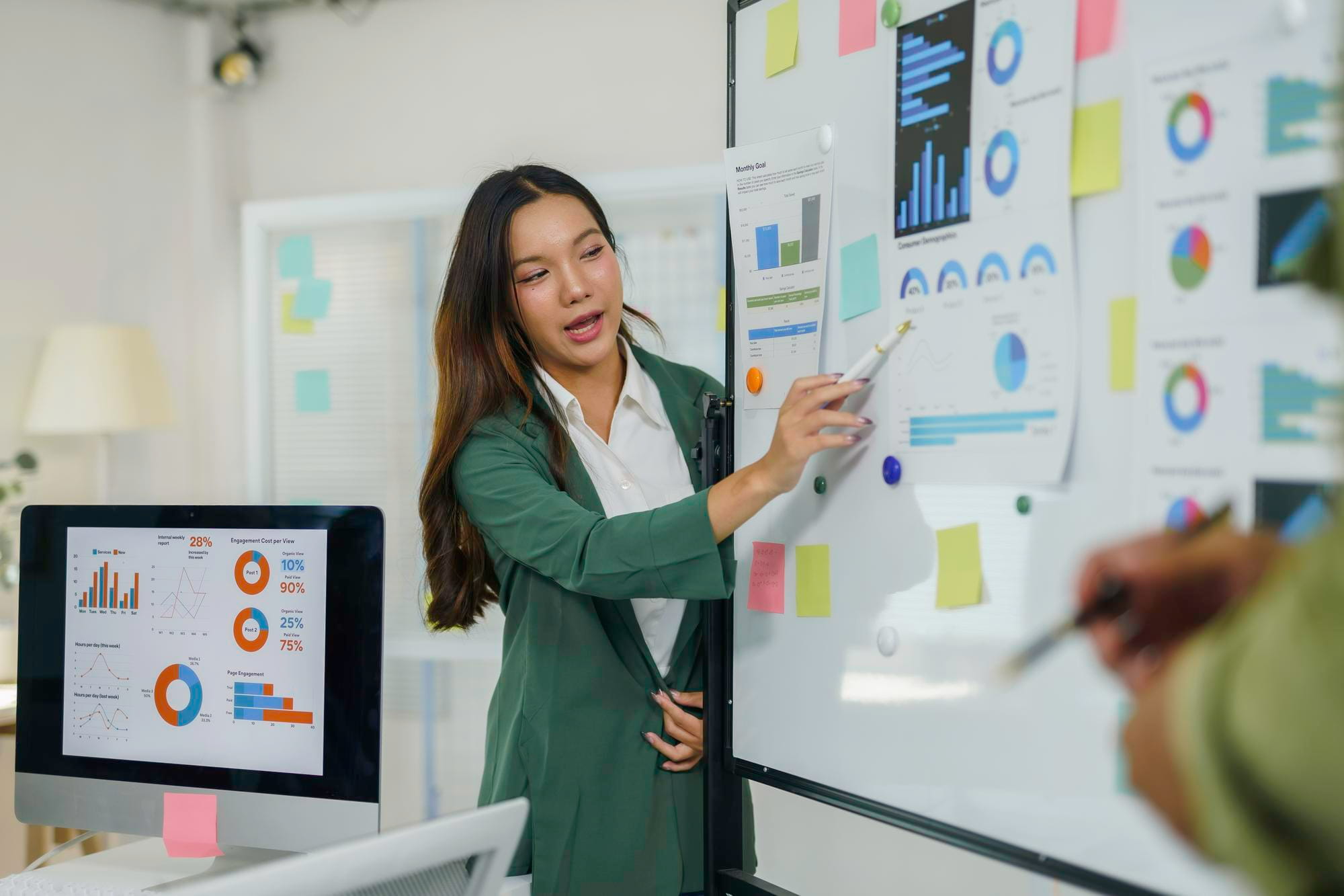 A manager pointing a pen at data charts and graphs pinned to a whiteboard during a presentation in an office.
